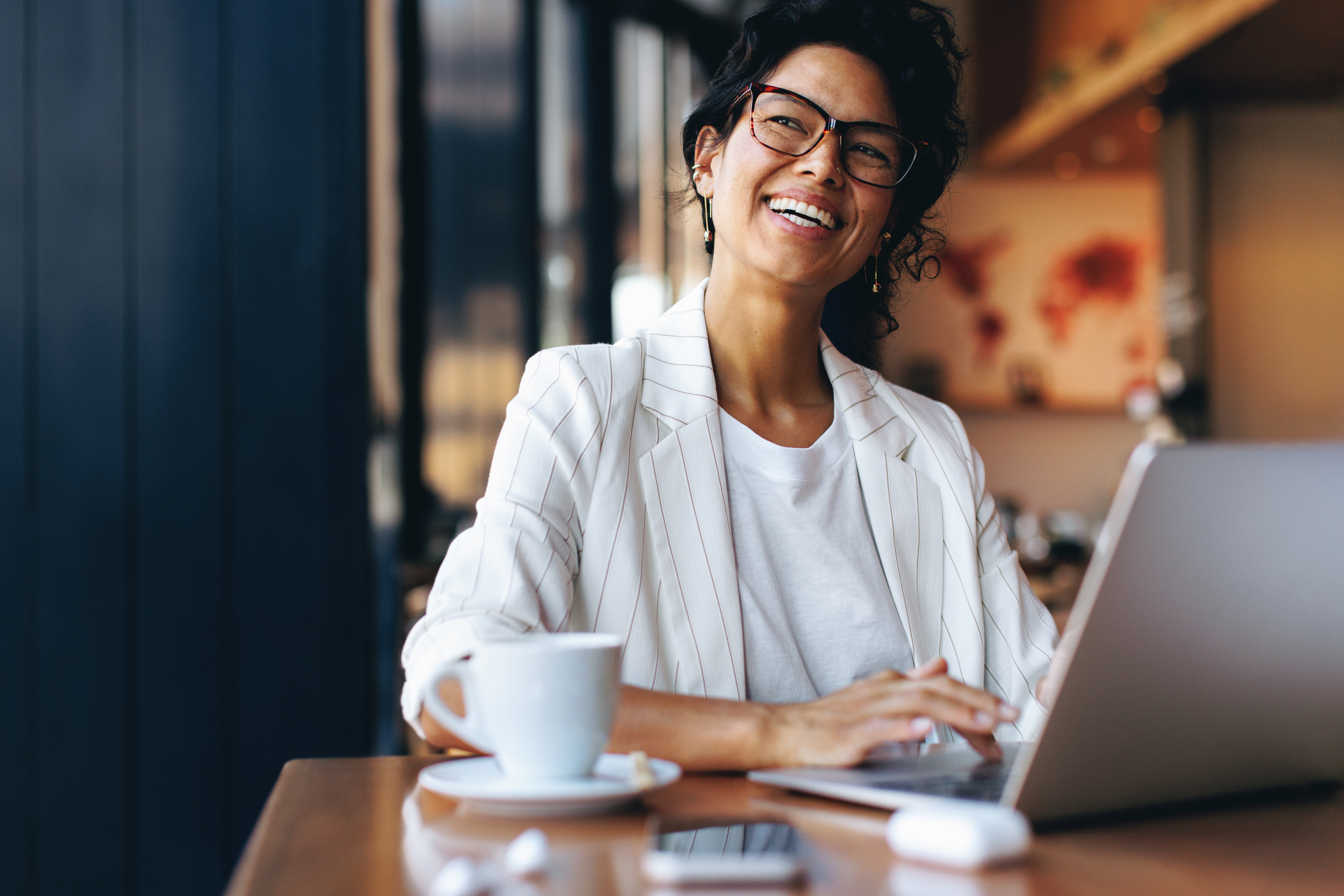 Happy businesswoman working remotely on laptop in a cozy cafe